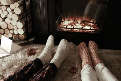 Couple in knitted socks near fireplace at home, closeup of legs