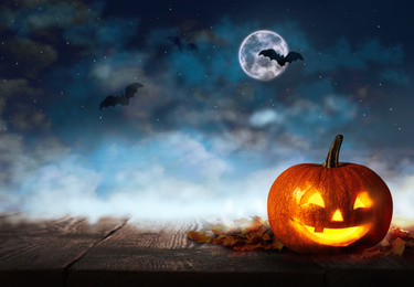 Spooky Jack O Lantern pumpkin under dark sky with flying bats and full moon on Halloween night. Space for text