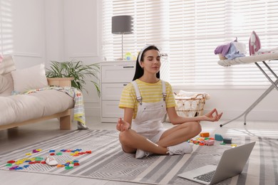 Photo of Calm young mother meditating on floor in messy living room