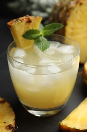 Photo of Delicious fresh pineapple juice with mint and ice cubes on black table, closeup