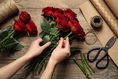 Woman making luxury bouquet of fresh roses at 
 wooden table, top view