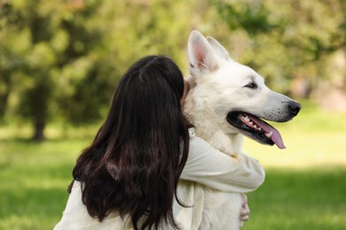 Young woman hugging her white Swiss Shepherd dog in park, back view