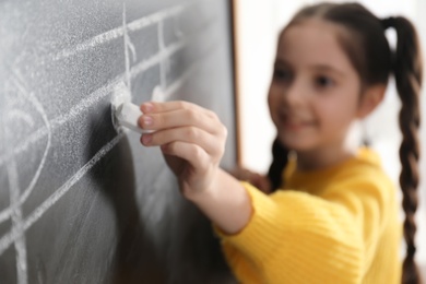 Little girl writing music notes on blackboard in classroom, closeup