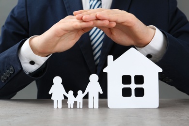 Man covering cutout paper family and house at table, closeup. Life insurance concept