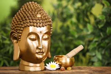 Buddha statue, lotus flower and singing bowl on wooden table. Space for text