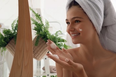 Beautiful teenage girl applying cleansing foam onto face near mirror at home. Skin care cosmetic