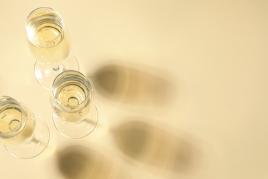 Photo of Glasses of delicious sparkling wine on light yellow background, above view. Space for text