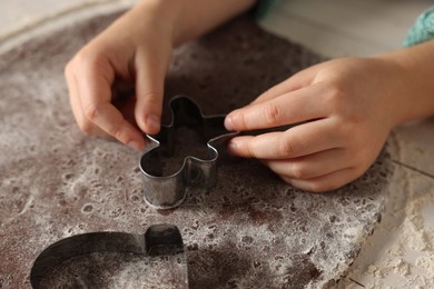 Little child cutting Christmas cookie at white wooden table, closeup