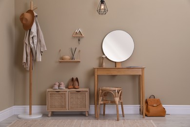 Modern hallway interior with stylish furniture, round mirror and wooden hanger for keys on beige wall
