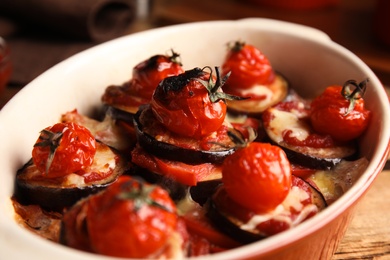 Baked eggplant with tomatoes and cheese in dishware on table, closeup