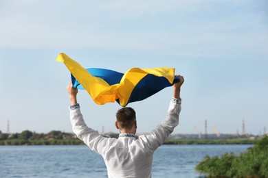 Man in vyshyvanka with flag of Ukraine outdoors, back view