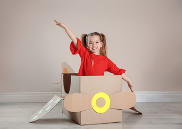 Cute little child playing with cardboard plane near beige wall