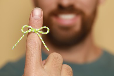 Man showing index finger with tied bow as reminder against beige background, focus on hand