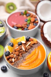 Photo of Bowl of delicious fruit smoothie with fresh orange slices, blueberries and granola on white table