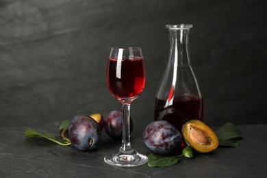 Delicious plum liquor and ripe fruits on black table. Homemade strong alcoholic beverage
