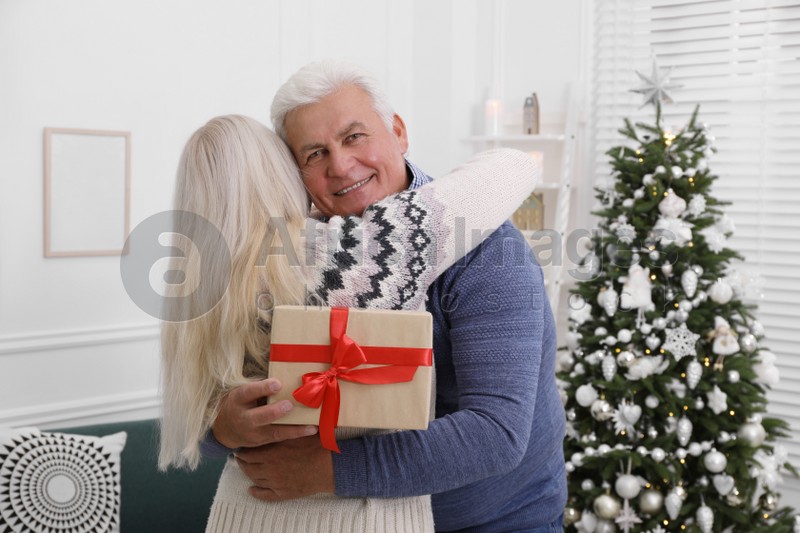 Happy mature couple with gift box hugging at home. Christmas celebration