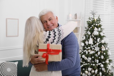 Happy mature couple with gift box hugging at home. Christmas celebration
