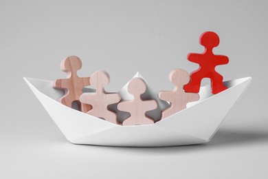 Red figure among wooden ones in paper boat on white background. Recruiter searching employee