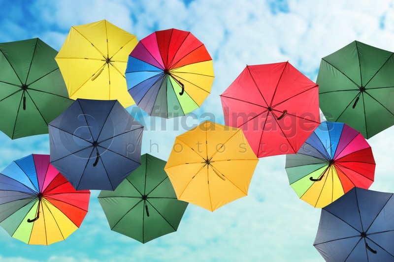 Group of different colorful umbrellas against blue sky with white clouds on sunny day, bottom view