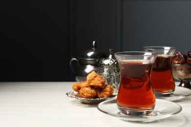Photo of Glasses of tea, baklava and date fruits served in vintage tea set on white wooden table, space for text