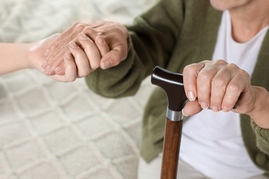 Caregiver and elderly woman with walking cane at home, closeup
