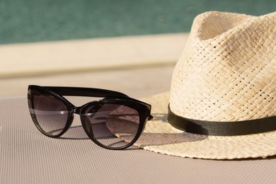 Stylish hat and sunglasses near outdoor swimming pool on sunny day