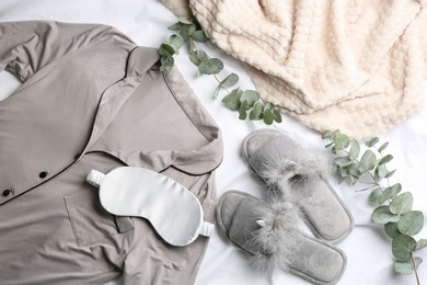 Flat lay composition with fluffy slippers and pajamas on white bedsheet. Comfortable home outfit