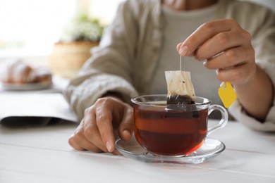 Woman taking tea bag out of cup at white wooden table indoors, closeup. Space for text