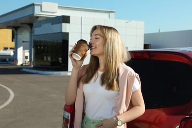 Photo of Beautiful young woman drinking coffee near car at gas station