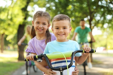 Happy siblings and their parents riding bicycles in park