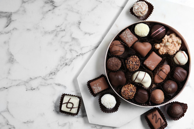 Different tasty chocolate candies on white marble table, flat lay. Space for text