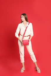 Beautiful young woman in casual outfit with stylish bag on red background
