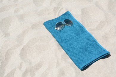 Soft blue towel and sunglasses on sandy beach, space for text