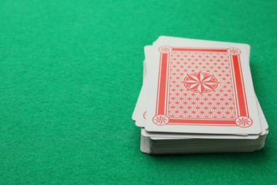 Photo of Deck of playing cards on green table, closeup. Space for text