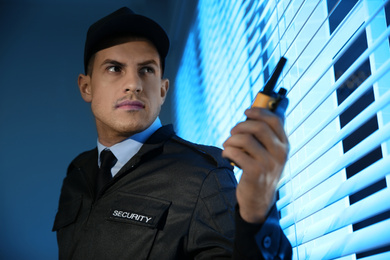 Professional security guard with portable radio set near window in dark room