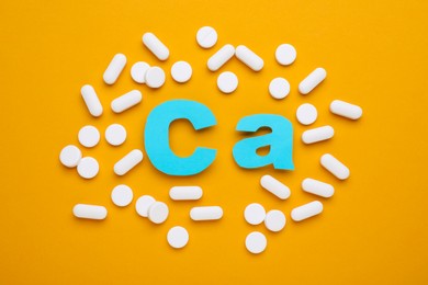 Pills and calcium symbol made of light blue letters on orange background, flat lay