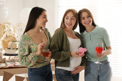 Happy pregnant woman with her friends holding tasty cookie and drinks at baby shower party