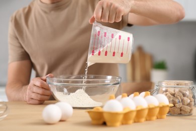 Photo of Man pouring flour into bowl at table in kitchen, closeup. Online cooking course
