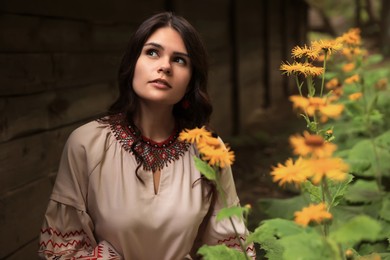 Photo of Beautiful woman wearing embroidered dress in blooming garden. Ukrainian national clothes