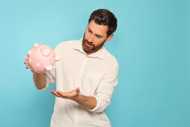Photo of Man with ceramic piggy bank on light blue background