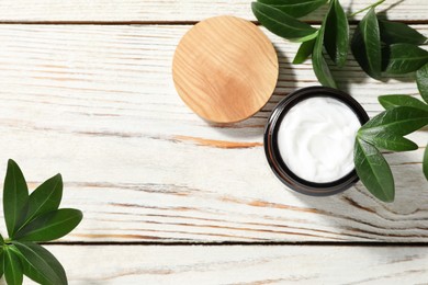 Jar of face cream and green leaves on wooden table, flat lay. Space for text