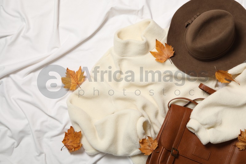 Photo of Flat lay composition with warm sweater and dry leaves on white fabric. Autumn season