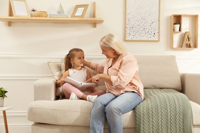 Happy grandmother with her granddaughter reading book together at home