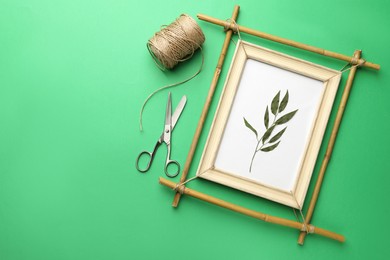 Bamboo frame with dried plant, scissors and twine on green background, flat lay. Space for text