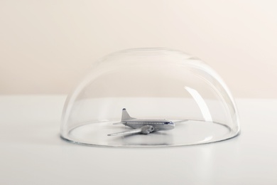 Toy plane under glass dome on white table. Travel insurance concept