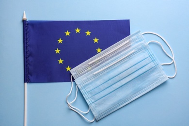 European Union flag and protective masks on light blue background, flat lay. Coronavirus outbreak