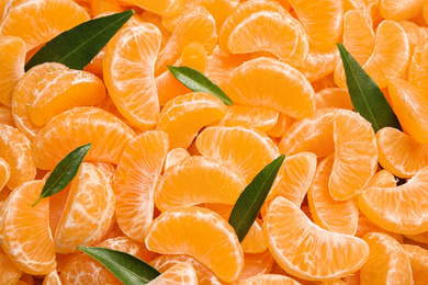 Photo of Fresh juicy tangerine segments with green leaves as background, top view