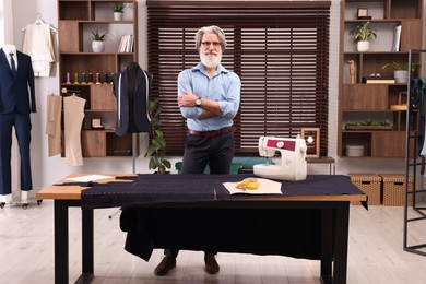 Professional tailor near table with equipment in workshop