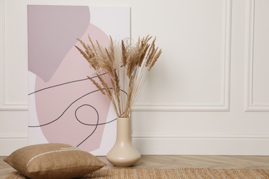 Fluffy reed plumes and painting near white wall indoors, space for text. Interior elements