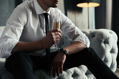 Photo of Businessman with glass of champagne on sofa indoors, closeup. Luxury lifestyle
